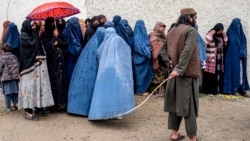 Cотрудник службы безопасности Талибана стоит на страже, пока афганские женщины в парандже стоят в очереди под проливным дождем, чтобы получить продукты питания, пожертвованные во время священного месяца Рамадан, Кабул, 25 марта 2025 года. Фото AFP